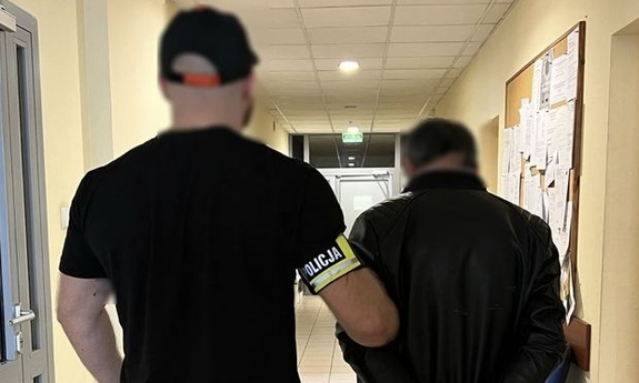funkcjonariusz z zatrzymanym zakutym w kajdanki na korytarzu